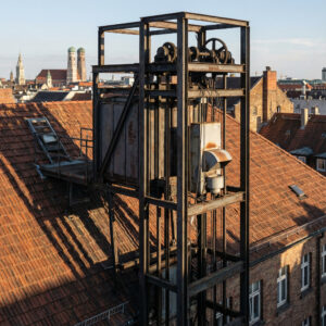 Eine massive, aufdringliche Stahlschacht-Konstruktion durchbricht die gemeinschaftliche Dachfläche eines Mehrfamilienhauses.